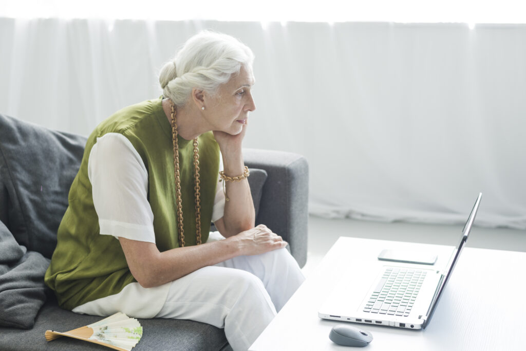 Starsza kobieta siedzi przy ławie z komputerem