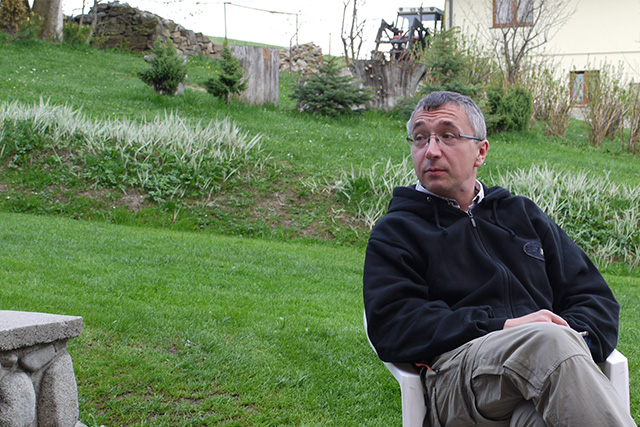 Zdjęcie mężczyzny w okularach i czarnej bluzie siedzącego na fotelu w ogrodzie