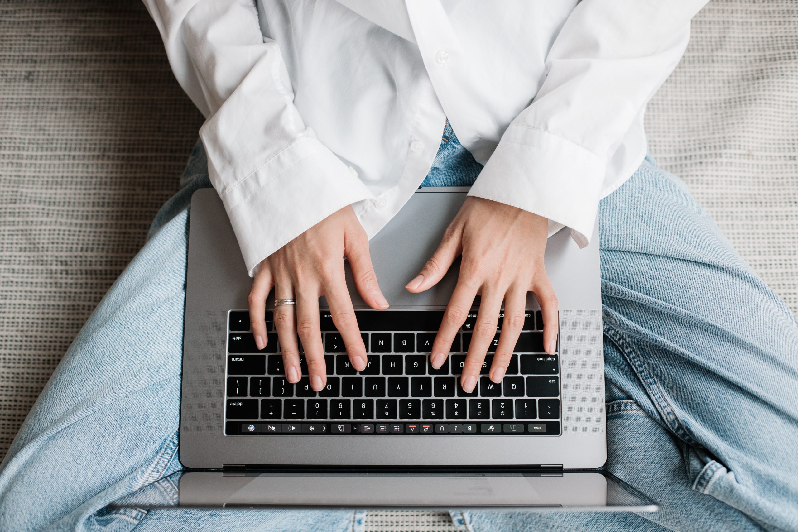 Dłonie kobiety oparte na klawiaturze laptopa, którego trzyma na kolanach
