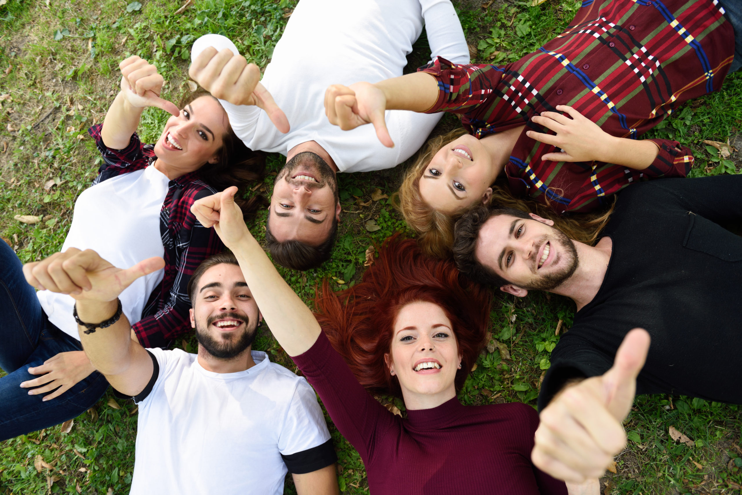 Grupa młodych ludzi leżących na trawie, trzymają kciuki w górę