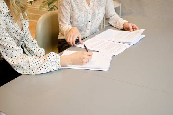 Dwie kobiety siedzące przy biurku. Jedna z nich wypełnia i podpisuje dokumenty.