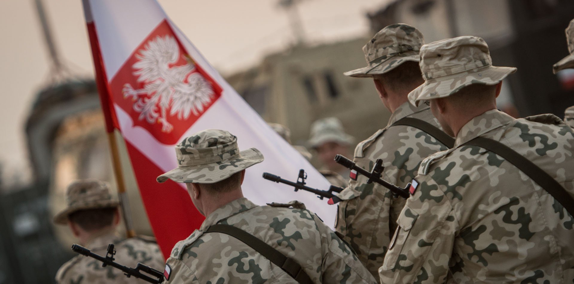 Żołnierze podczas pochodu. Jeden z nich niesie flagę Polski.