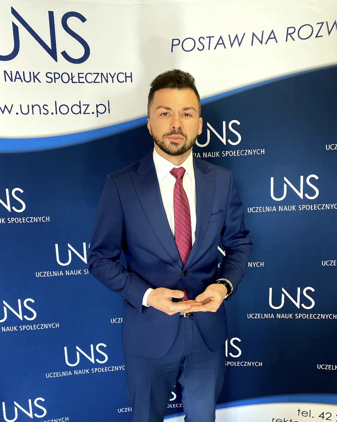 Zdjęcie młodego mężczyzny w garniturze na tle logotypów uczelni - Kamil Łuka