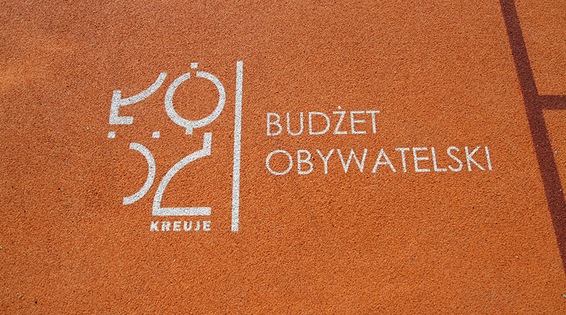 Zdjęcie powierzchni kredowej boiska z białym logiem Łódź kreuje i napisem Budżet obywatelski