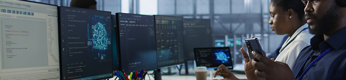 Ludzie siedzący przed rzędem monitorów z technologicznymi grafikami